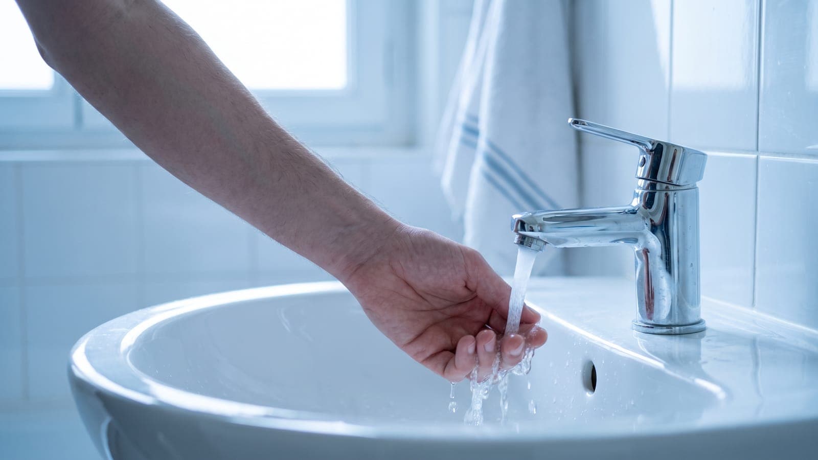 Main sous le robinet d'un lavabo pour vérifier si l'eau sort chaude